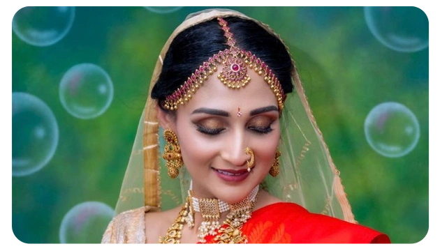 A woman in a traditional red saree adorned with intricate gold jewelry and a delicate veil, set against a backdrop of green and bubbles.