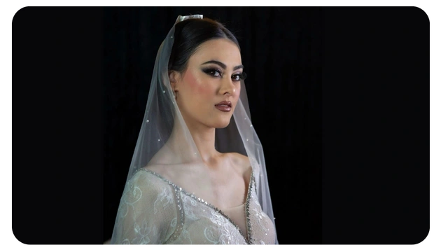 A woman in an elegant gown adorned with pearls and intricate lace, wearing a delicate veil against a dark background.