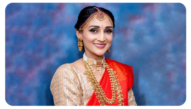 A woman dressed in a traditional Indian saree, adorned with gold jewelry, posed against a textured blue background.