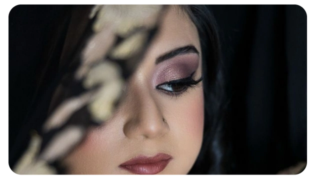A close-up of a person with dark hair, dressed in black, partially illuminated against a dark backdrop, creating a mysterious atmosphere.